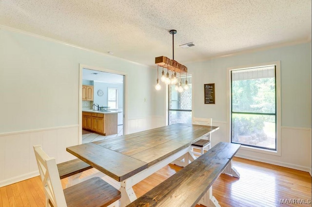 dining space with plenty of natural light, sink, light wood-type flooring, and a textured ceiling