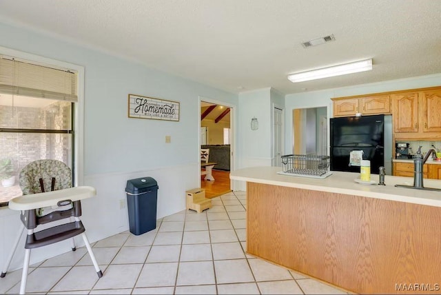 kitchen with light tile patterned floors, a textured ceiling, black fridge, and light brown cabinets