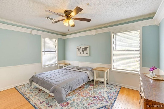 bedroom with multiple windows, light wood-type flooring, ceiling fan, and crown molding