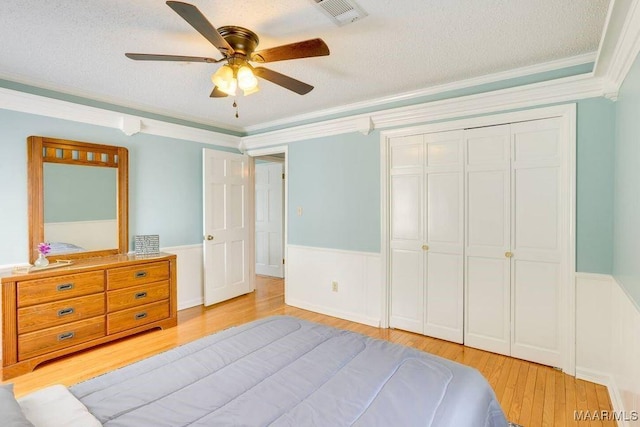 bedroom featuring ceiling fan, crown molding, a textured ceiling, a closet, and light wood-type flooring