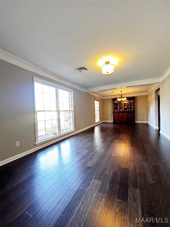 empty room featuring dark wood-type flooring, a chandelier, and ornamental molding