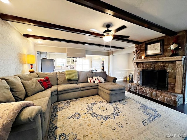 living room with a stone fireplace, ceiling fan, and beamed ceiling