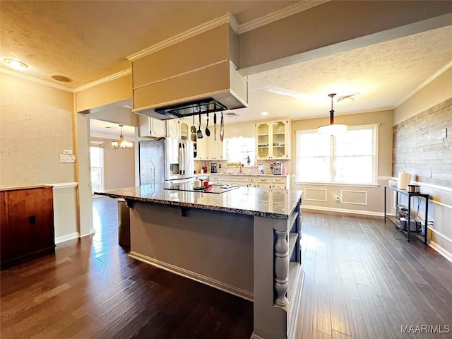 kitchen featuring stone countertops, stainless steel fridge, black electric cooktop, decorative light fixtures, and a kitchen island