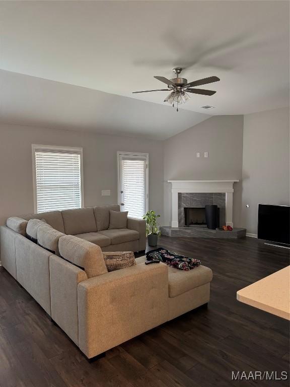 living room with dark hardwood / wood-style flooring, vaulted ceiling, ceiling fan, and a tiled fireplace