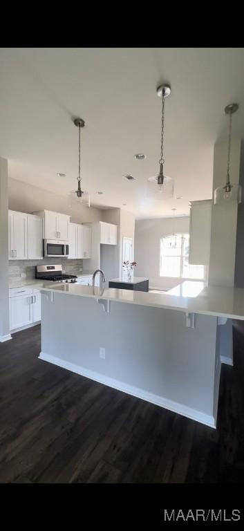 kitchen with white cabinets, hanging light fixtures, appliances with stainless steel finishes, tasteful backsplash, and dark hardwood / wood-style flooring