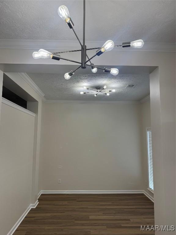 empty room with a textured ceiling, dark hardwood / wood-style floors, an inviting chandelier, and ornamental molding