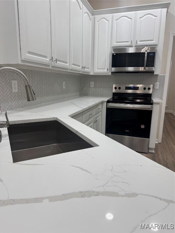 kitchen featuring appliances with stainless steel finishes, light stone counters, white cabinetry, and sink