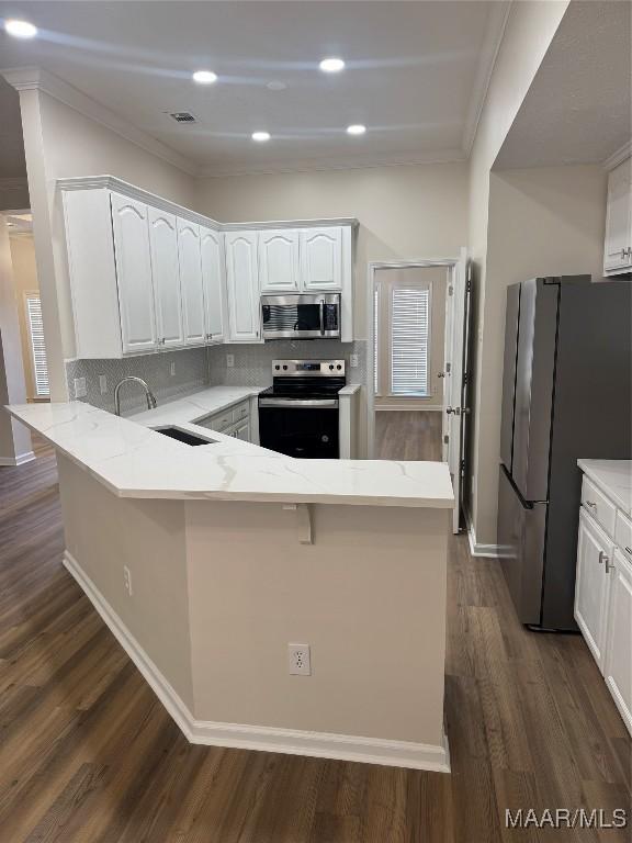 kitchen with kitchen peninsula, decorative backsplash, dark hardwood / wood-style floors, appliances with stainless steel finishes, and white cabinetry