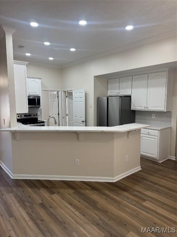 kitchen with kitchen peninsula, decorative backsplash, white cabinets, and appliances with stainless steel finishes