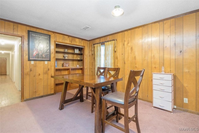 dining space with built in shelves, a textured ceiling, light colored carpet, and crown molding