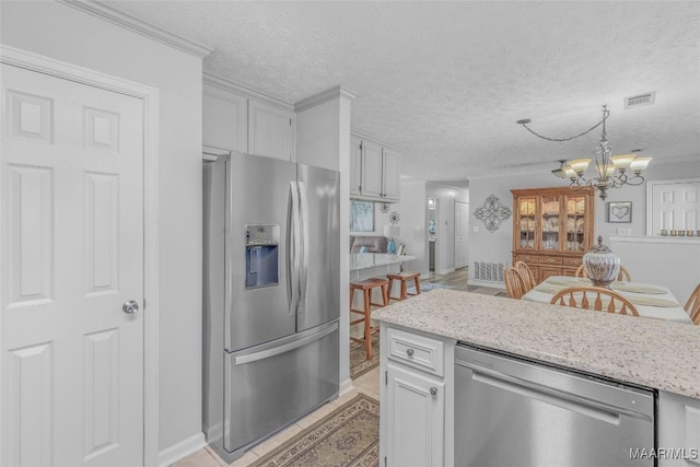 kitchen featuring hanging light fixtures, stainless steel appliances, a notable chandelier, a textured ceiling, and white cabinets