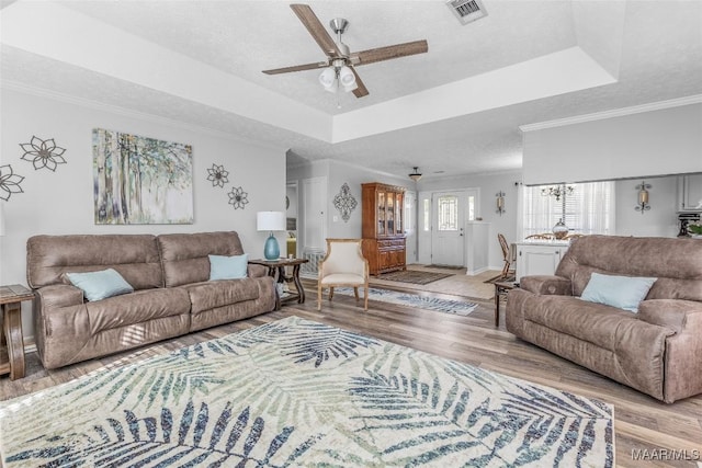 living room with a textured ceiling, light wood-type flooring, a tray ceiling, and crown molding