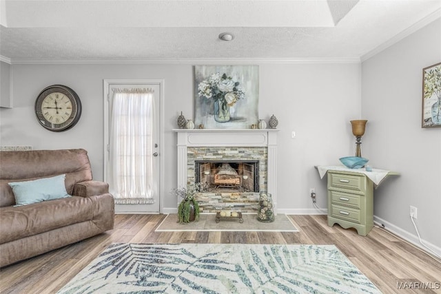 living room with a textured ceiling, light hardwood / wood-style floors, a stone fireplace, and ornamental molding