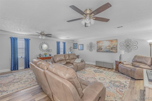 living room with ceiling fan, crown molding, light wood-type flooring, and a textured ceiling