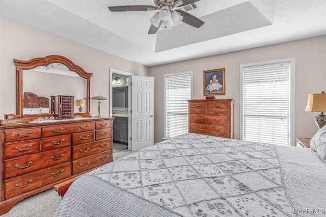 bedroom with ensuite bathroom, a raised ceiling, ceiling fan, a textured ceiling, and multiple windows