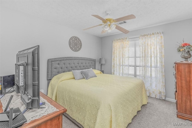 bedroom with ceiling fan, light colored carpet, and a textured ceiling