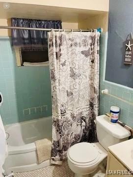 full bathroom with shower / tub combo with curtain, vanity, tile walls, and toilet