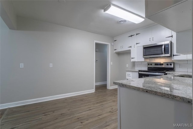 kitchen with white cabinetry, dark wood-type flooring, stainless steel appliances, light stone counters, and backsplash