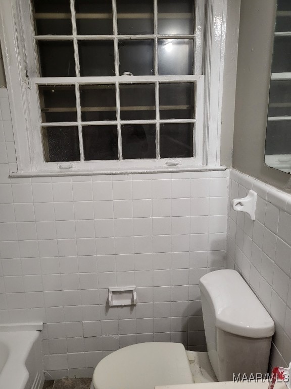 bathroom featuring a bath, toilet, and tile walls