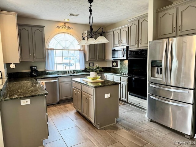 kitchen featuring a textured ceiling, stainless steel appliances, sink, decorative light fixtures, and a center island