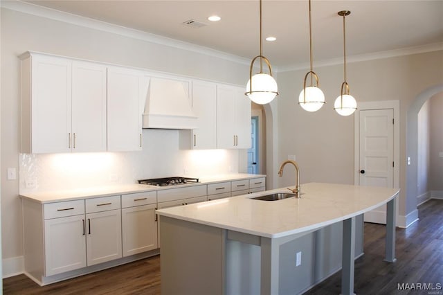 kitchen with pendant lighting, sink, white cabinets, a kitchen island with sink, and custom range hood