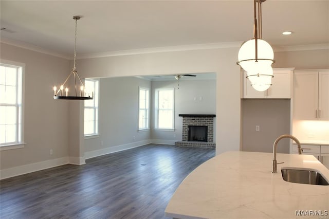 kitchen with sink, crown molding, a fireplace, light stone countertops, and white cabinets