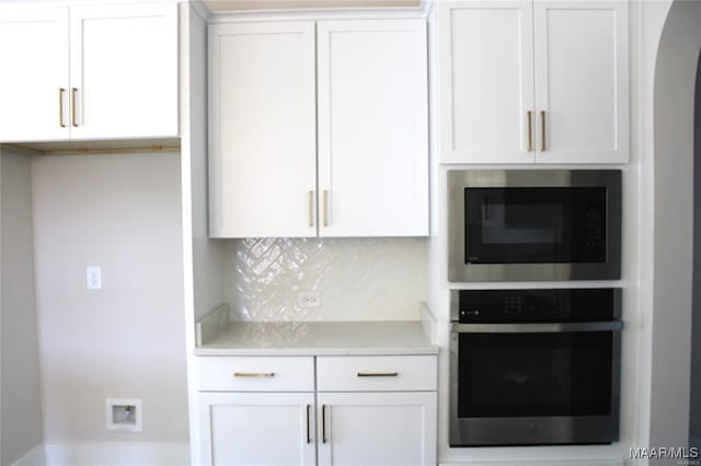 kitchen with white cabinetry, built in microwave, tasteful backsplash, and stainless steel oven