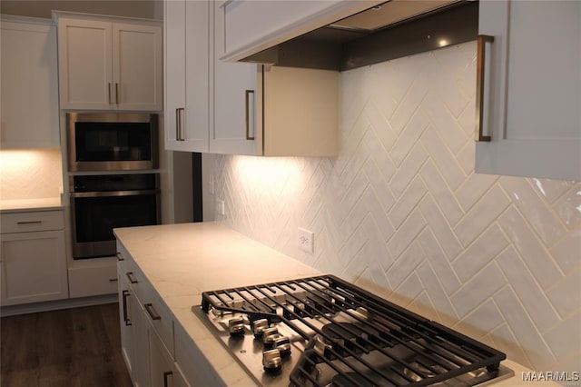 kitchen featuring built in microwave, decorative backsplash, stainless steel oven, gas stovetop, and light stone countertops