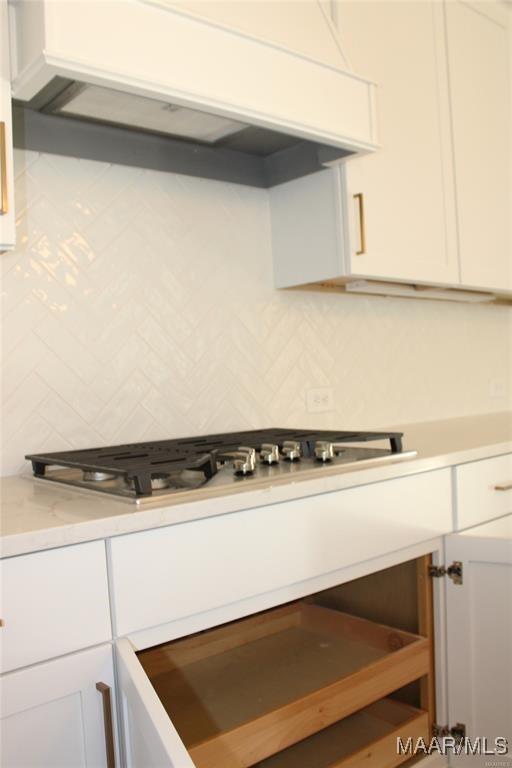 details with tasteful backsplash, premium range hood, stainless steel gas cooktop, and white cabinets