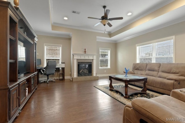 living room with a tile fireplace, ceiling fan, dark hardwood / wood-style floors, crown molding, and a tray ceiling