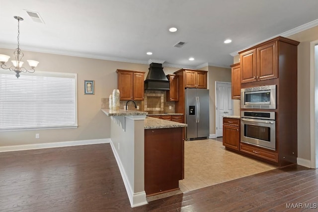 kitchen with kitchen peninsula, ornamental molding, custom range hood, stainless steel appliances, and hanging light fixtures