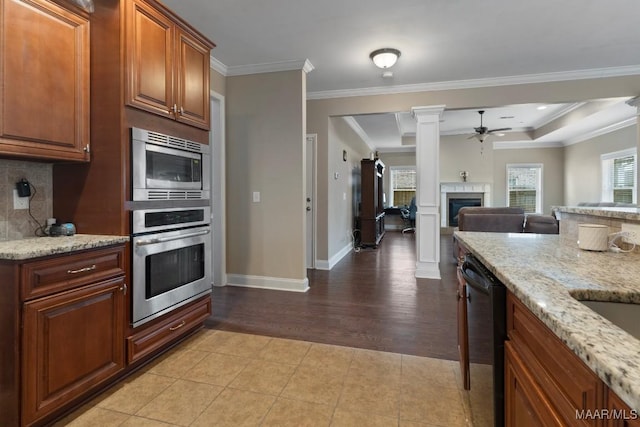 kitchen with crown molding, ceiling fan, appliances with stainless steel finishes, light stone counters, and a tiled fireplace