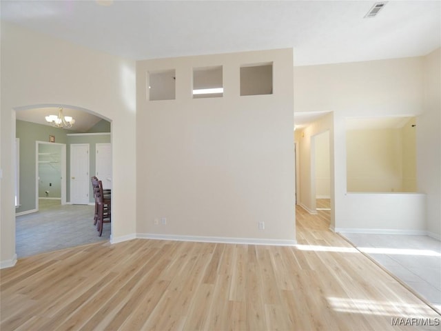 empty room featuring light hardwood / wood-style floors, a high ceiling, and an inviting chandelier