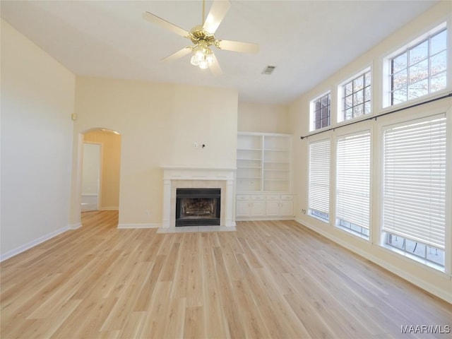 unfurnished living room featuring ceiling fan, a wealth of natural light, light wood-type flooring, and a tile fireplace