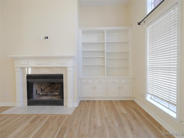 unfurnished living room with built in shelves, light wood-type flooring, and a tiled fireplace