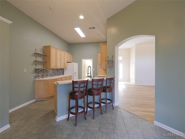 kitchen with white refrigerator with ice dispenser, light brown cabinetry, tasteful backsplash, kitchen peninsula, and a breakfast bar area