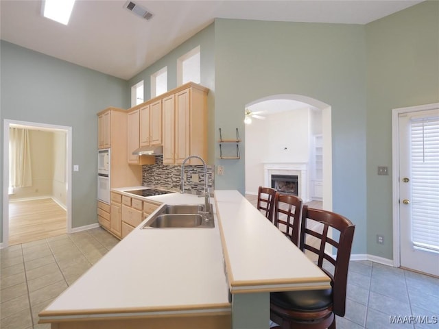 kitchen featuring kitchen peninsula, light brown cabinetry, decorative backsplash, and sink