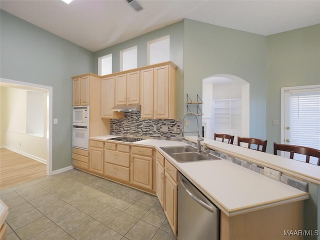 kitchen featuring a towering ceiling, light brown cabinetry, white appliances, and sink