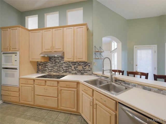 kitchen featuring sink, light brown cabinets, a high ceiling, tasteful backsplash, and white appliances