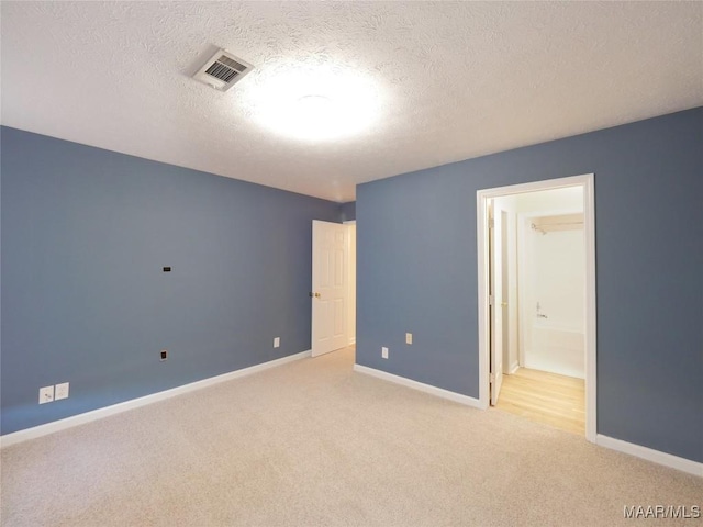 unfurnished bedroom with ensuite bathroom, light colored carpet, and a textured ceiling