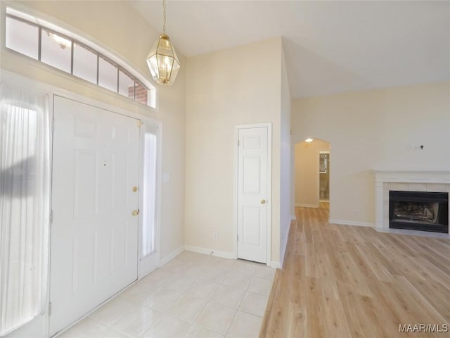 foyer featuring light hardwood / wood-style floors, a fireplace, high vaulted ceiling, and an inviting chandelier