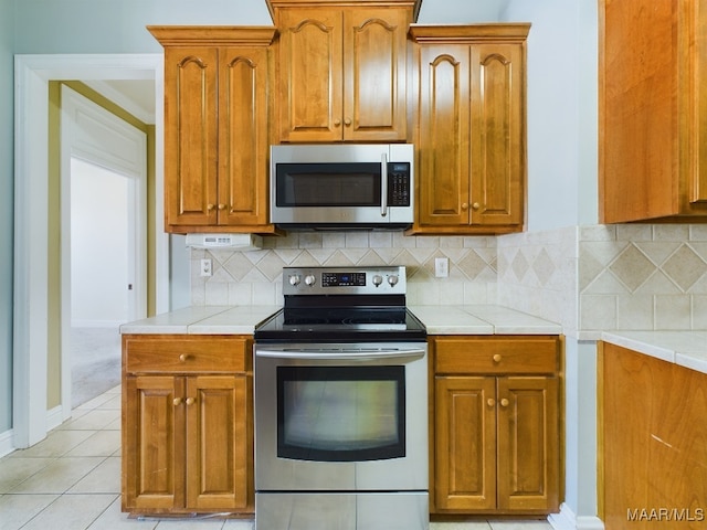 kitchen featuring backsplash, light tile patterned flooring, and stainless steel appliances