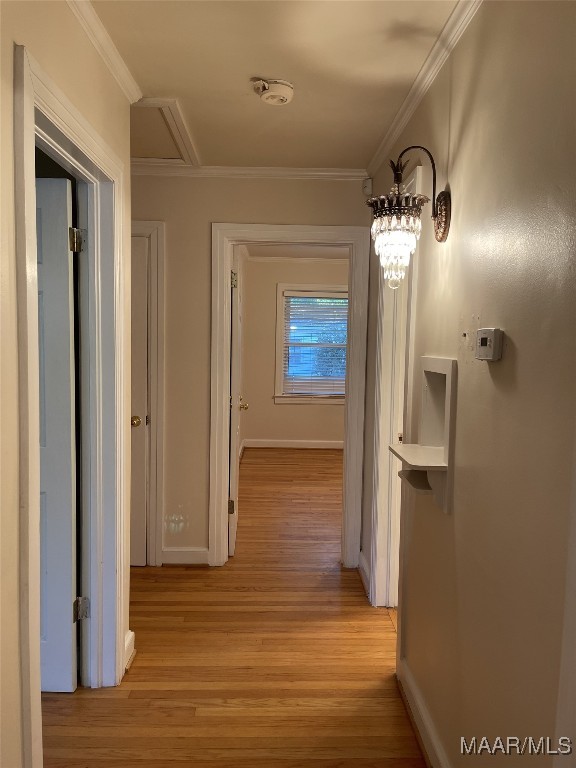 hallway featuring an inviting chandelier, crown molding, and light hardwood / wood-style flooring