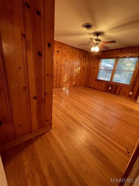 empty room with ceiling fan, wood walls, and light wood-type flooring