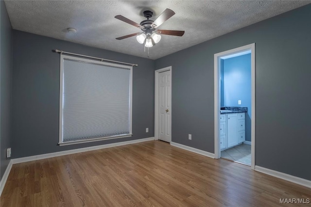 unfurnished bedroom featuring ceiling fan, light wood-type flooring, a textured ceiling, and connected bathroom