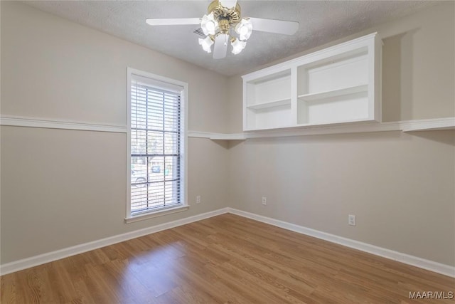 empty room featuring built in shelves, ceiling fan, hardwood / wood-style floors, and a textured ceiling