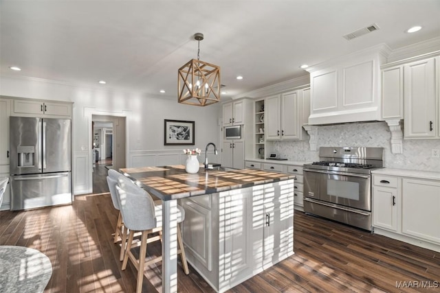 kitchen featuring appliances with stainless steel finishes, sink, a center island with sink, white cabinets, and butcher block countertops