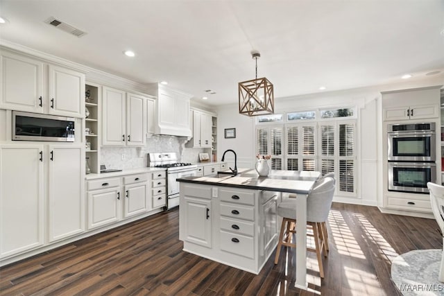 kitchen featuring appliances with stainless steel finishes, sink, a center island with sink, white cabinetry, and hanging light fixtures