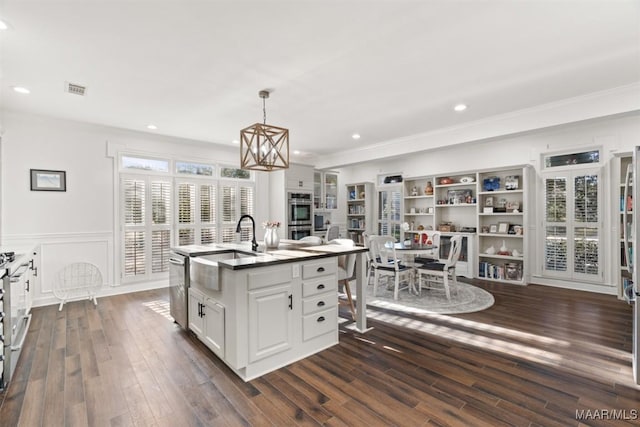 kitchen featuring pendant lighting, white cabinets, dark hardwood / wood-style floors, an island with sink, and stainless steel appliances