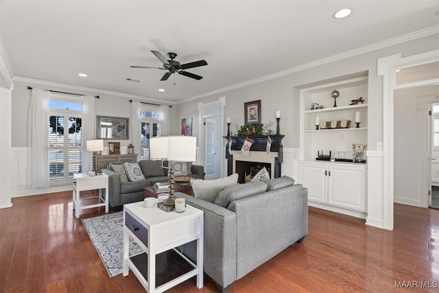 living room featuring built in shelves, dark wood-type flooring, ceiling fan, and ornamental molding